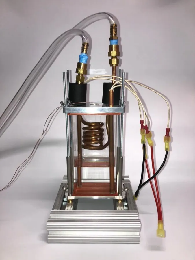 La cámara de transferencia de calor: un tubo de vidrio entre placas de aluminio, con un serpentín condensador de cobre y dos varillas de cobre que alojan los calentadores de cartucho, con termopares y cables de potencia conectados.