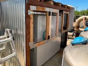 Oxygen concentrator cabinets under a corrugated shelter beside stainless water tanks