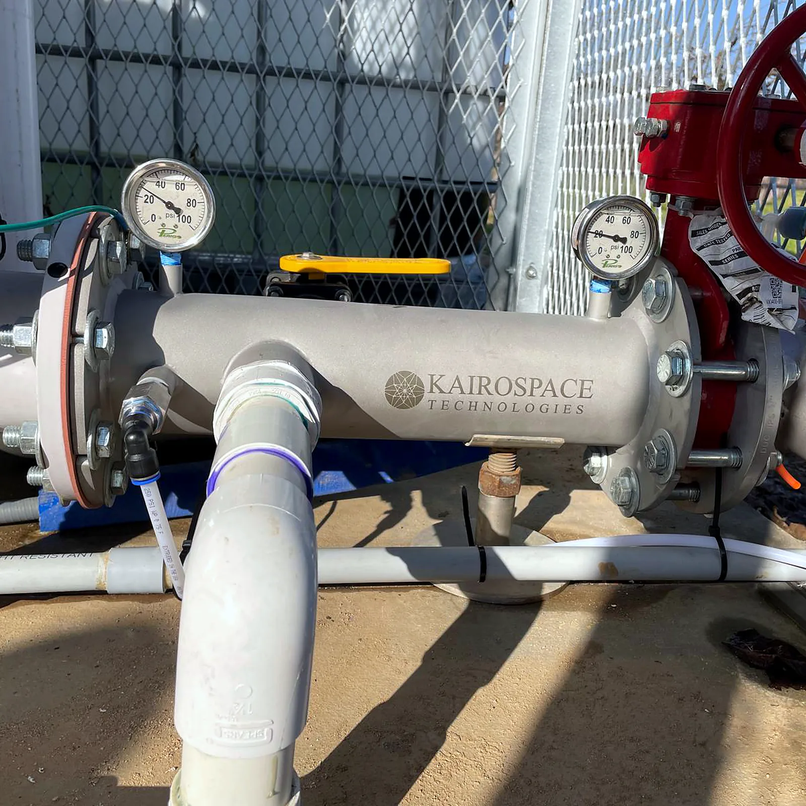Injector installed between flanges at a fenced pump station, pressure gauges on both ends and a gate valve downstream