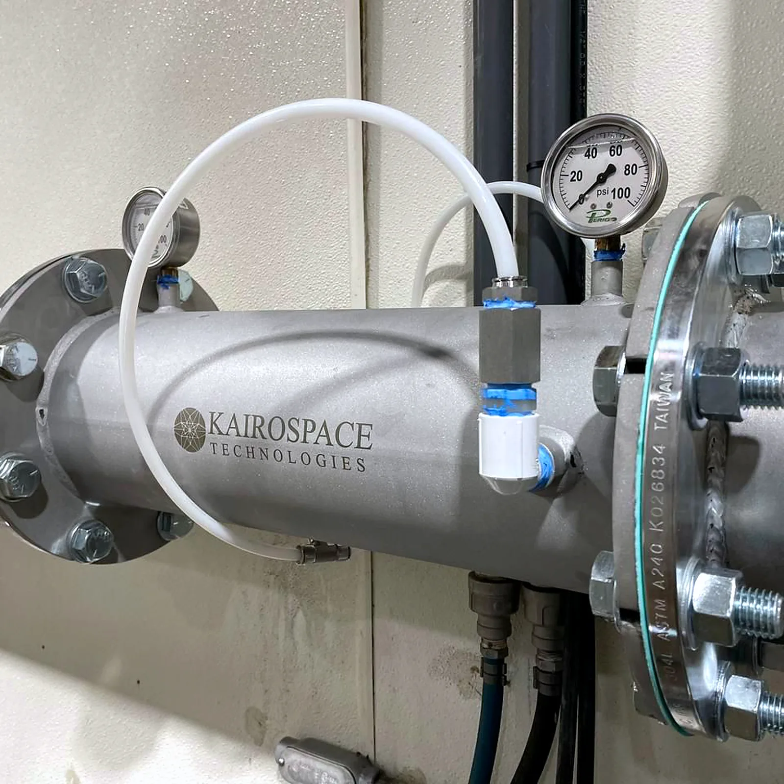 Close-up of an injector with a white oxygen feed line entering through a compression fitting, pressure gauge above the flange