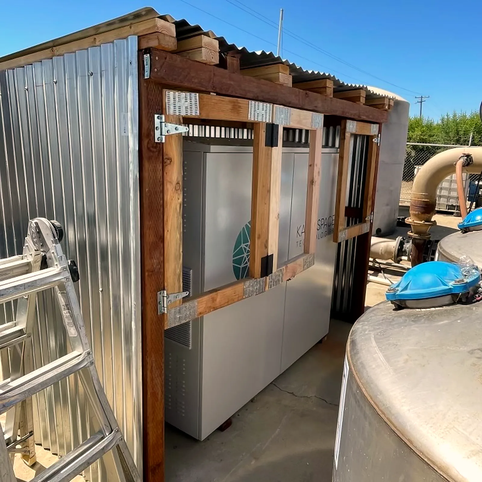 Oxygen concentrator cabinets under a purpose-built corrugated shelter beside stainless water tanks