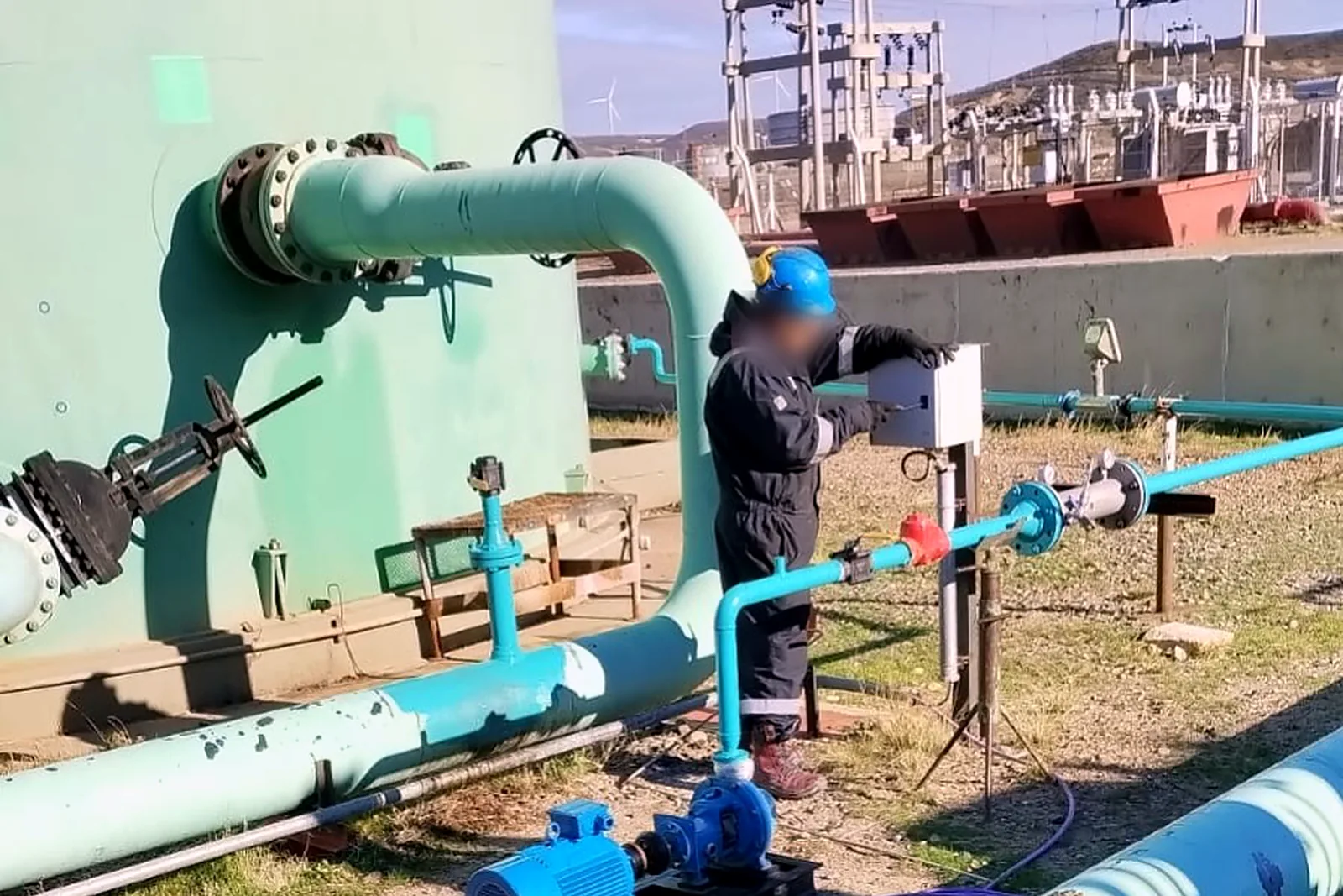 Operator adjusting a control panel beside the injection line at a tank battery, with a pump skid in the foreground