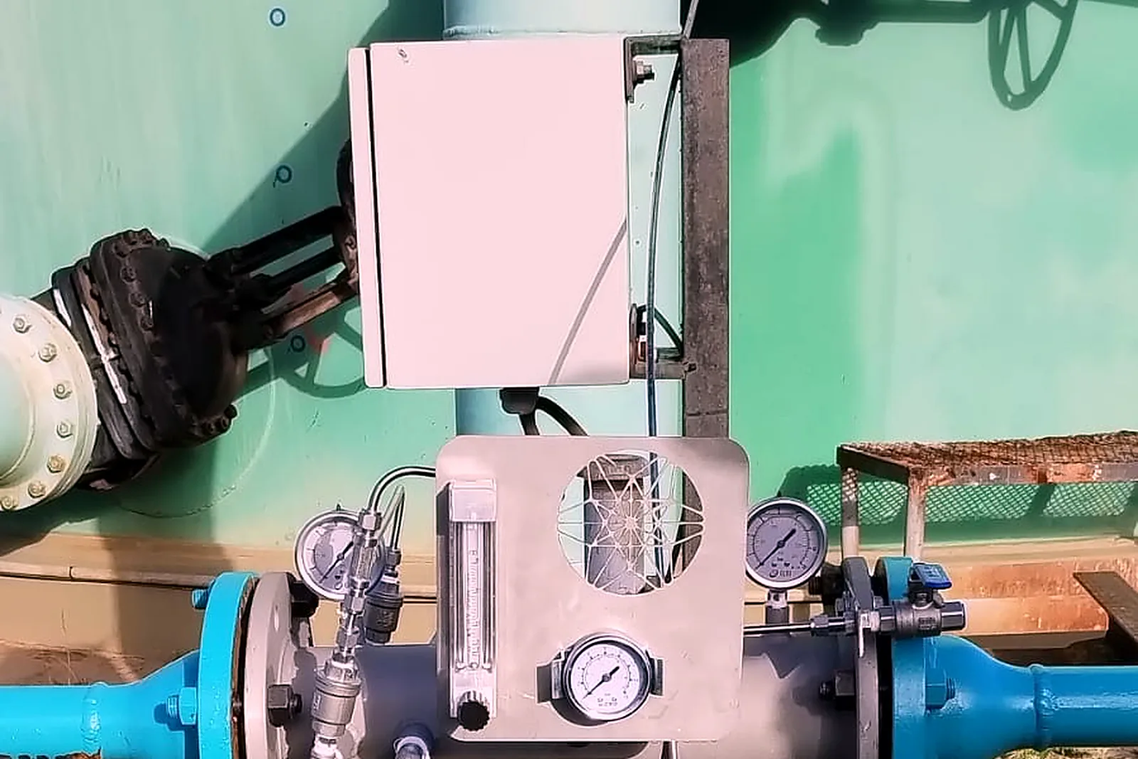 Control enclosure and flow meter mounted above an injector installed in the line at the base of a storage tank
